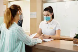 physical-therapist-with-face-mask-writing-data-her-client-reception-desk-_1_